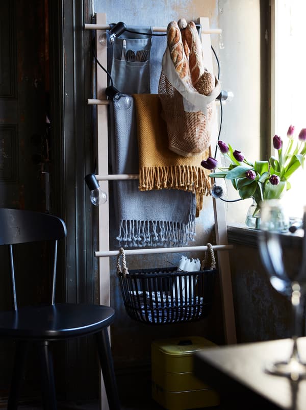 A towel stand is propped against a wall and used as extra storage. Throw blankets and baskets hang from it.