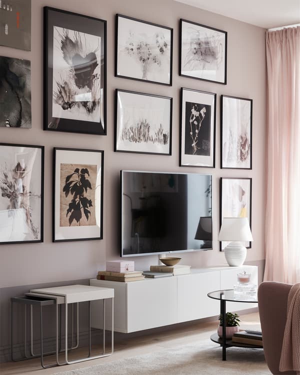 A traditional living room gallery wall, full of pictures in black KNOPPÄNG frames, behind a TV on a low, white TV bench.