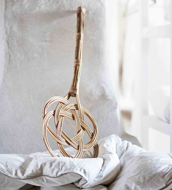 A traditional rattan carpet beater stands against a white wall.