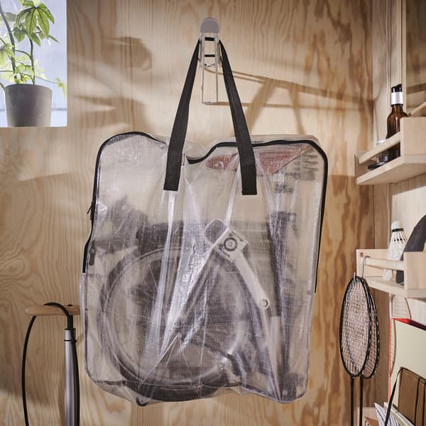 A transparent DIMPA storage bag with a foldable bicycle inside is hanging on a hook that’s mounted on a wooden wall.