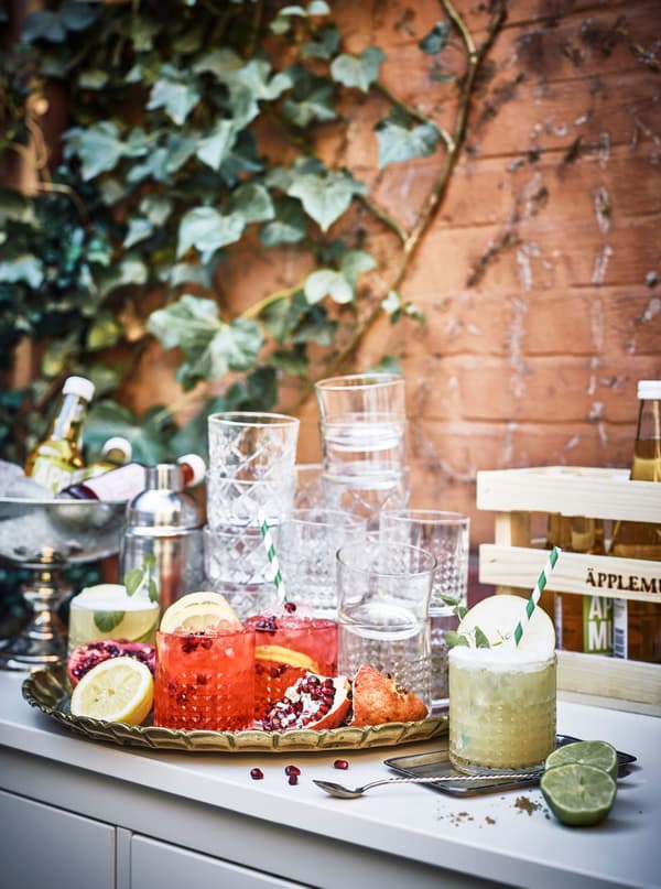A tray of cocktails and beautiful glasses sit on top of a chest of drawers in a courtyard.