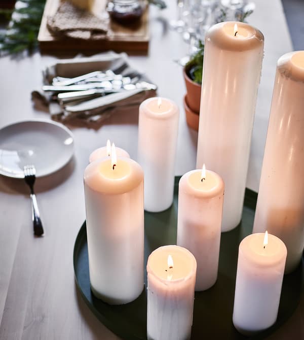 A tray of lit, tall, white candles set on a prepped buffet table.