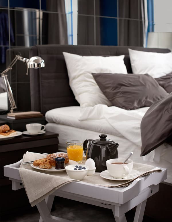A tray table set with breakfast sits beside a large, cosy bed.