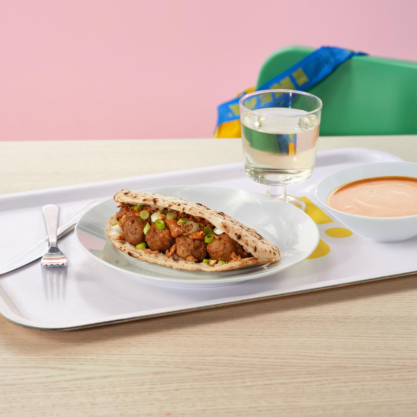 A tray with a pita bread with meatballs, tomato soup, and fruit water.