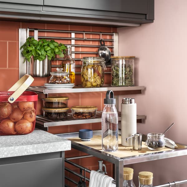 A trolley and a suspension rail with a wall grid/shelves in stainless steel, food in glass jars and onions in a red basket.