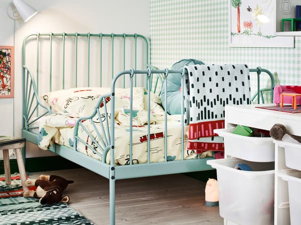 A turquoise MINNEN extendable bed in the corner of a children’s room, lined with toys, reading light and storage.
