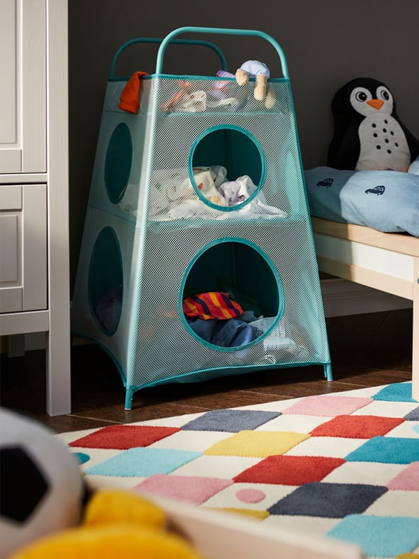 A turquoise TIGERFINK storage with compartments is placed beside a chest of drawers in a child's room. Each of its compartments is filled with toys and clothes.