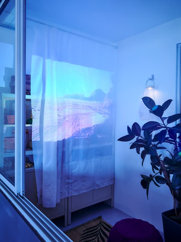 À une extrémité d’un balcon, un film est projeté sur un rideau de douche BJÄRSEN blanc suspendu à une tringle BOTAREN.