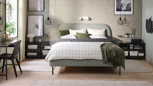 A VADHEIM upholstered bed with VITKLÖVER bed linen stands in a bedroom. VITTSJÖ TV benches stand at the sides of the bed.