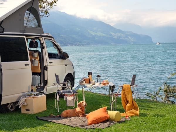 A van parked by the lake with a table and folding chairs next to it.