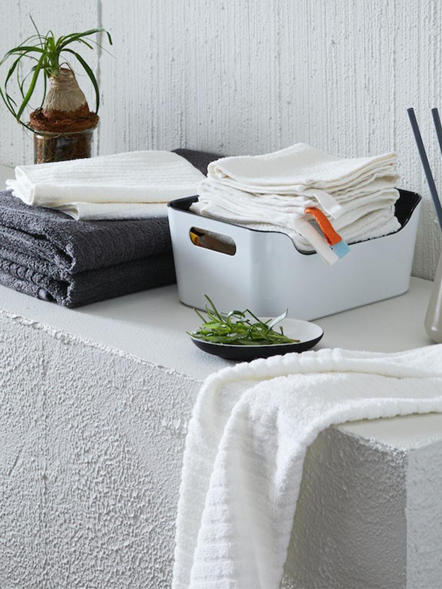 A VARIERA box in white and black is placed in the bathroom alongside other items. It is filled with neatly-folded hand towels.