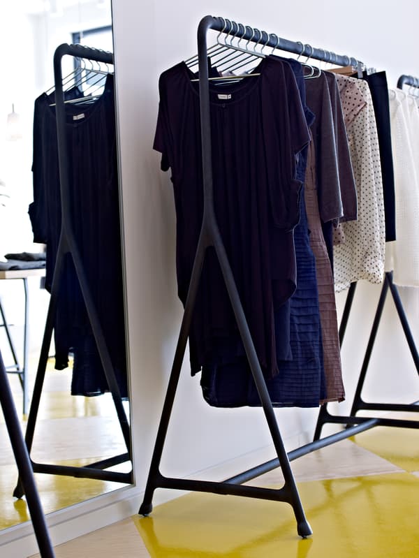 A variety of clothes hang on hangers on a TURBO clothes rack near a mirror in a room with white walls.