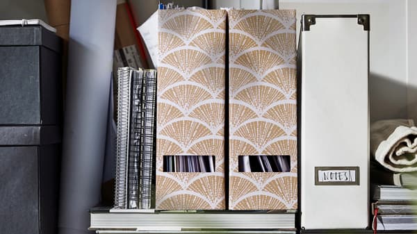 A variety of IKEA magazine files are placed on top of a couple of books. A few notebooks are leaning against them.