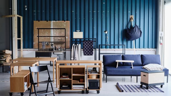 A variety of RÅVAROR furnishings including tables, a day-bed and storage units are set against a teal zinc plate wall.