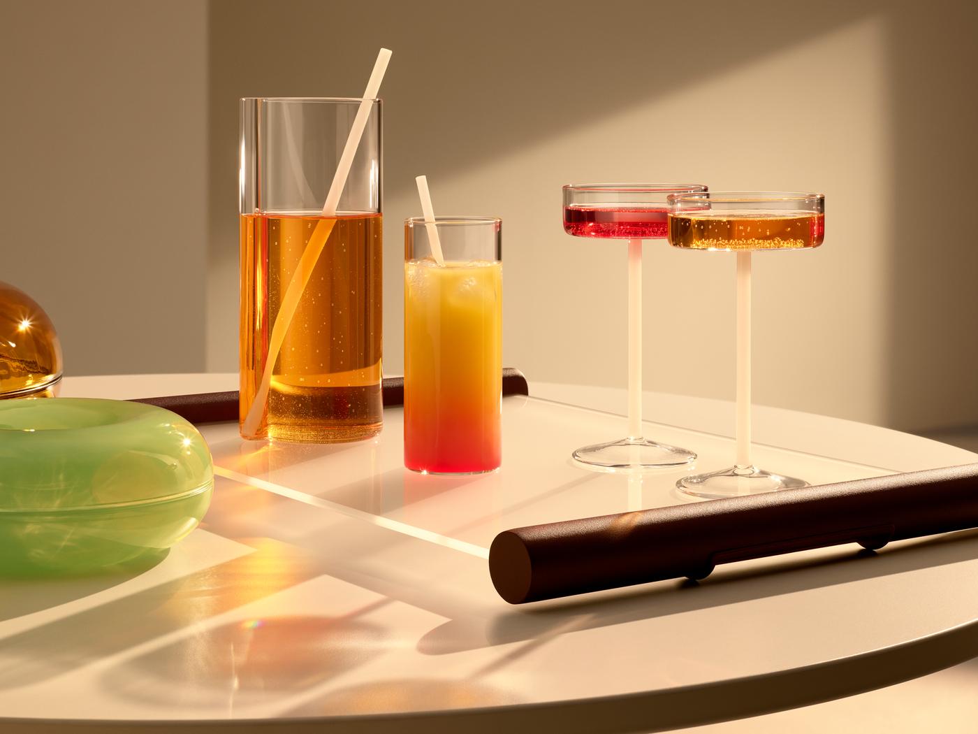 A VARMBLIXT carafe and glasses are on a VARMBLIXT glass tray on a table, with VARMBLIXT doughnut-shaped glass serving bowls.