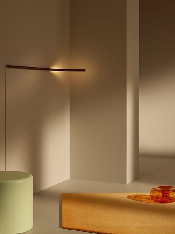 A VARMBLIXT linear wall lamp is mounted horizontally onto a wall in a minimal space, with a VARMBLIXT rug and coffee tables.