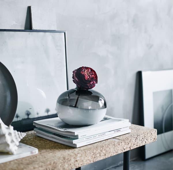 A vase on a shelf with a paper rose.
