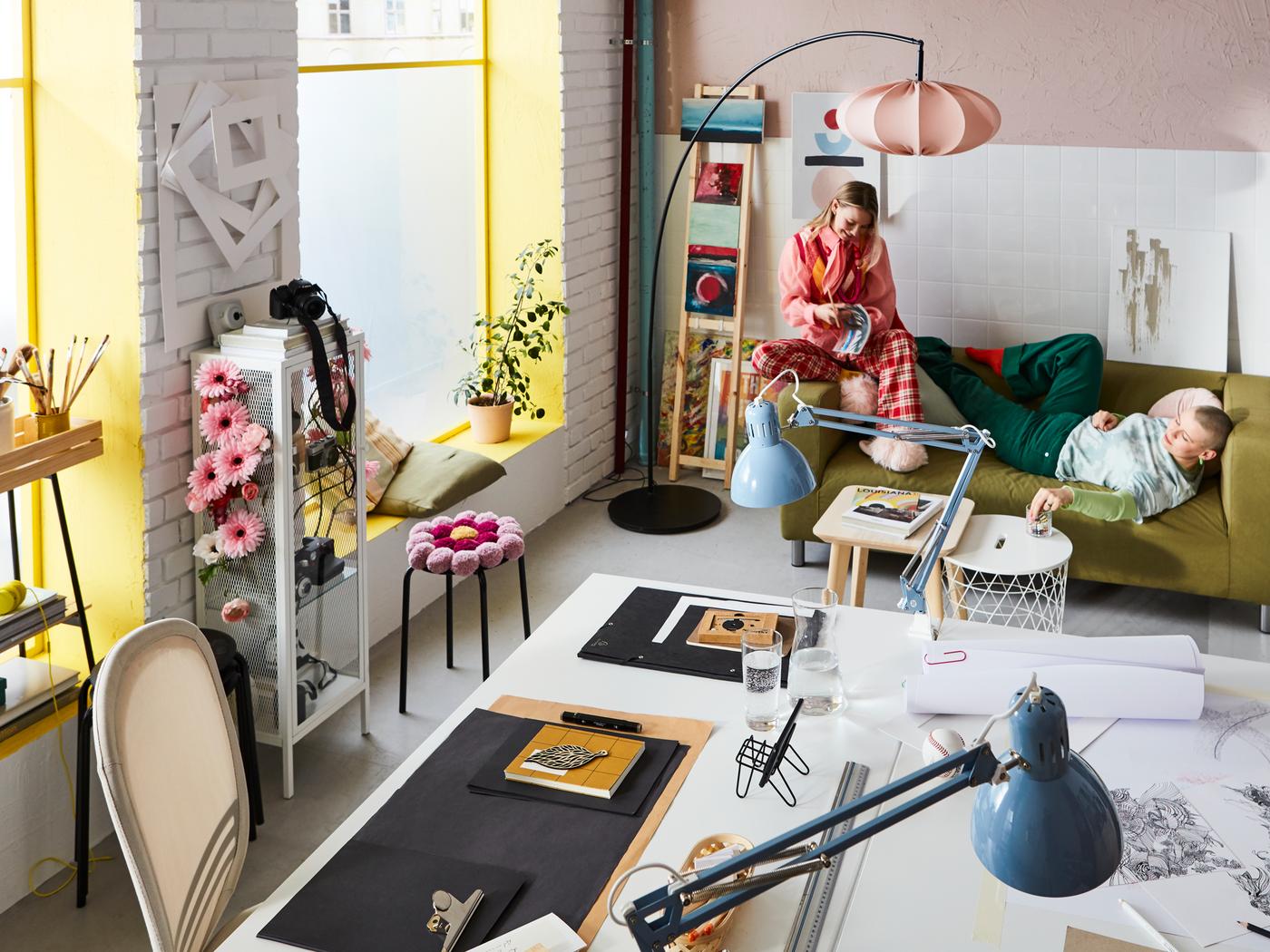 A vibrant, colourful workspace and living area with two young women taking a break on a KLIPPAN sofa.