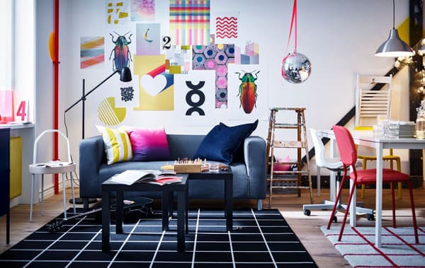A vibrant living room and workspace with wall art, sofa, coffee tables, lamps, white tables, chairs, rugs and an old ladder.
