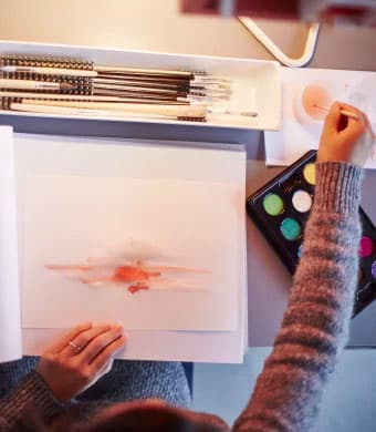 A view from above of someone painting on some white paper on a grey desk