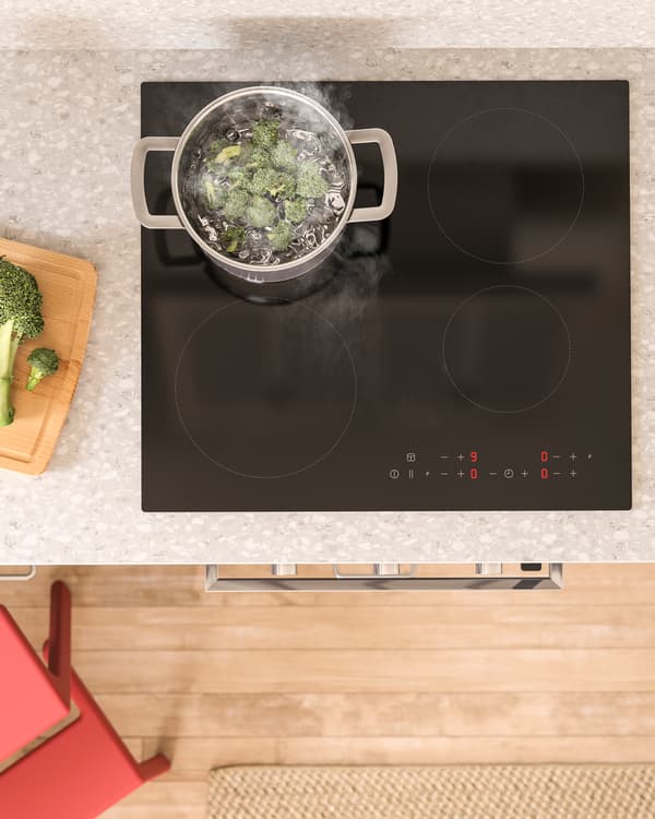 A view from above with MATMÄSSIG black induction hob, a saucepan is placed on it and broccoli is being boiled in it.