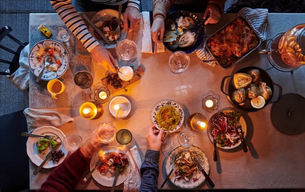 A view of a dining table set for a meal with a monochrome tablecloth and an informal mix of dinnerware, linens, and candles.