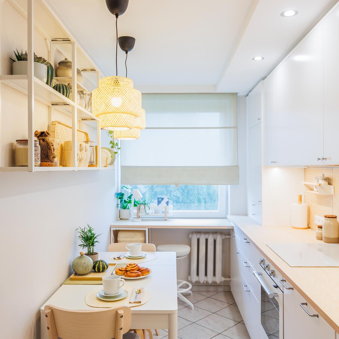 A view of a kitchen after a makeover, featuring white cabinets, light wooden accents and minimalist decor. A table is set with breakfast, and the space appears bright, tidy and modern.