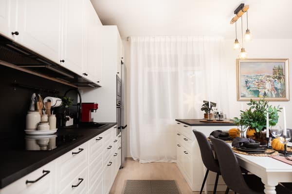 A view of the kitchen work area with a stove, oven, and appliances, next to a dining table and a window with curtains.