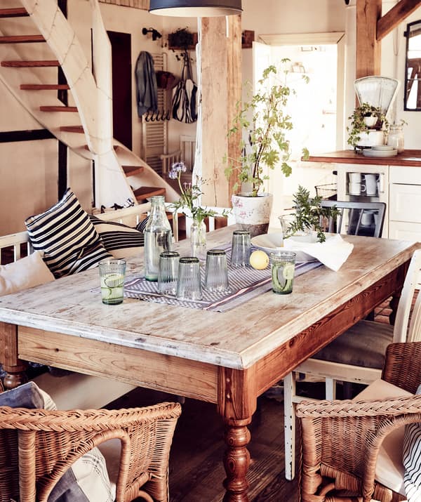 A vintage wooden dining table with rattan armchairs in an open living space.