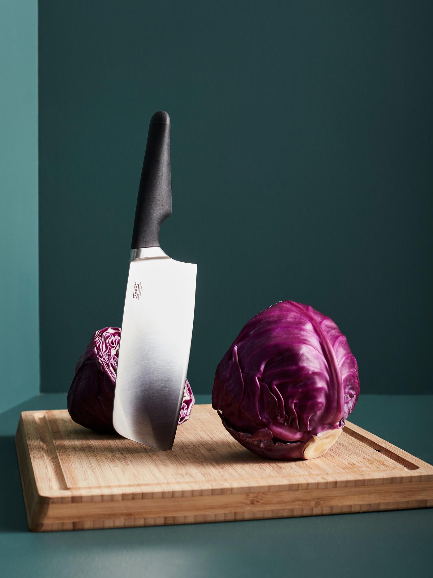 A VÖRDA Chinese chopper with a black handle stands vertically on an APTITLIG butchers block in bamboo next to red cabbage.