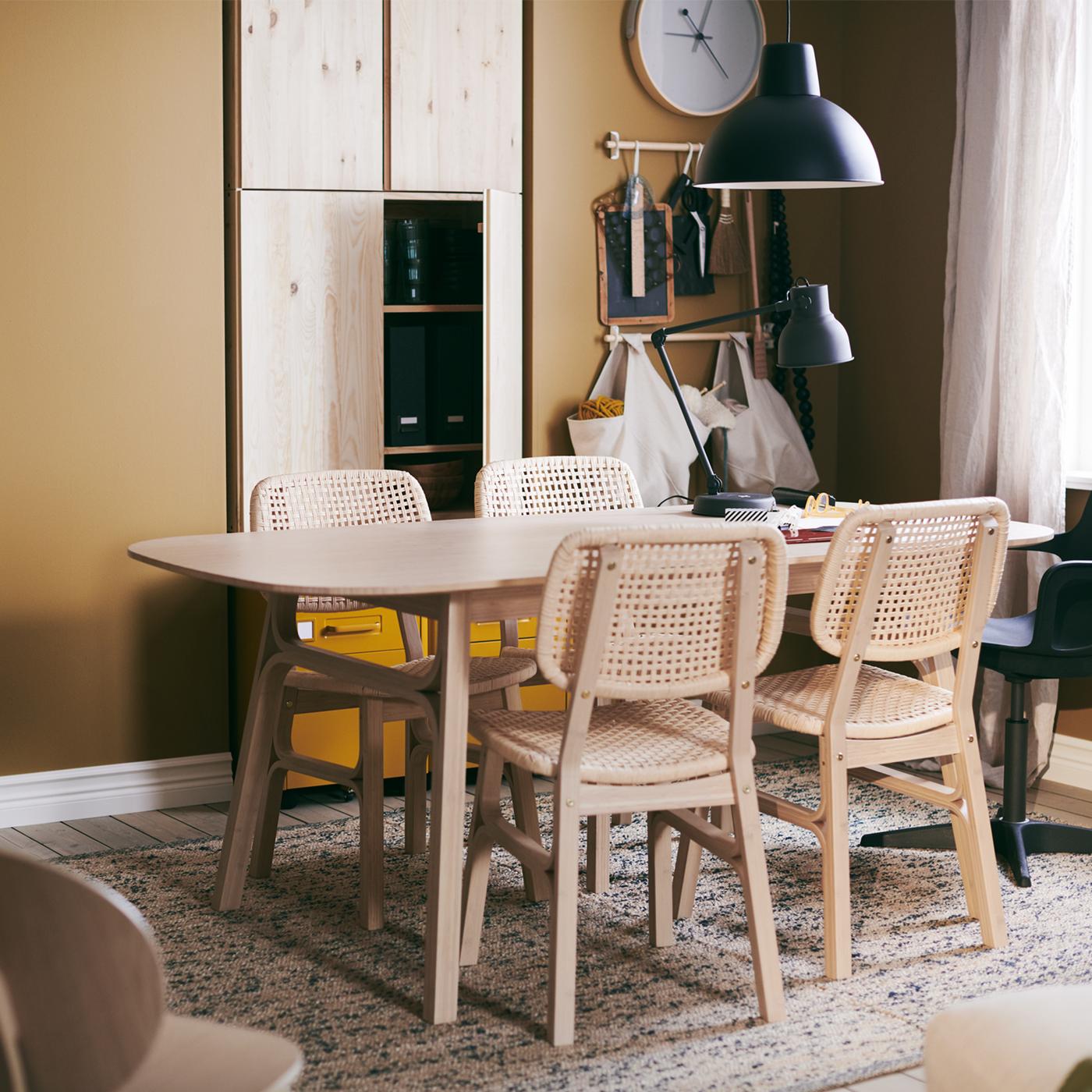A VOXLÖV table with four chairs, standing on a MELHOLT flatwoven rug, a ROTBLÖTA wall clock on the wall and a hanging lamp.