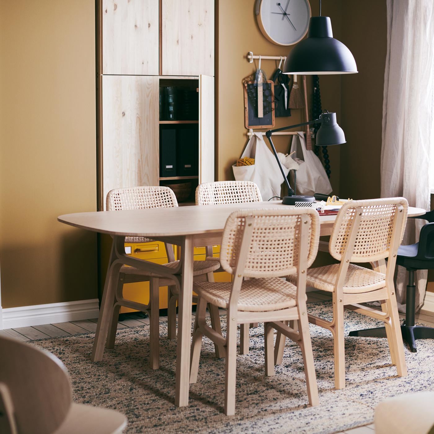 A VOXLÖV table with four chairs, standing on a MELHOLT flatwoven rug, a ROTBLÖTA wall clock on the wall and a hanging lamp.