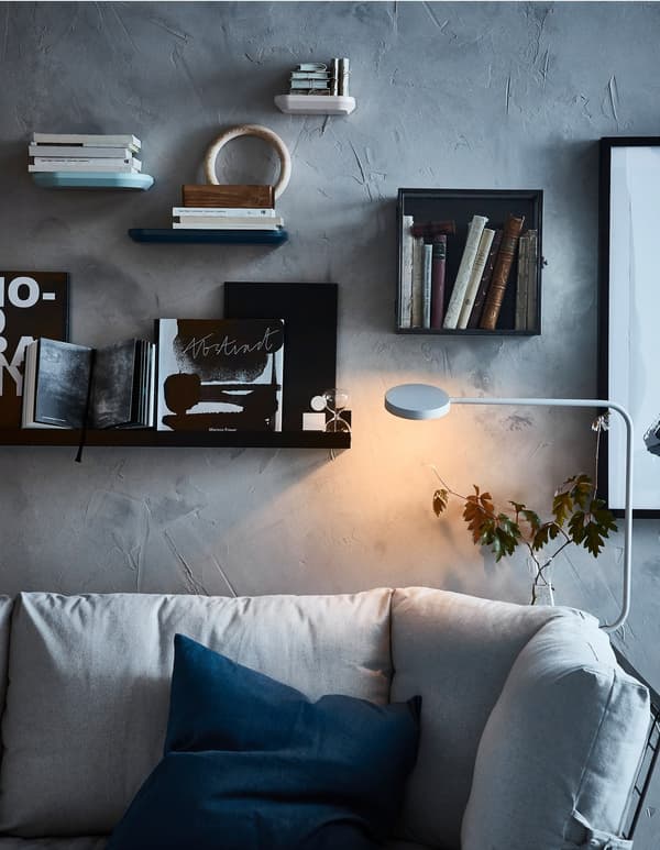 A wall behind a sofa decorated with display boxes and picture ledges loaded with books and pictures.