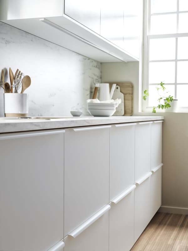 A wall in a kitchen with a line of base cabinets underneath a work top and wall cabinets above it.
