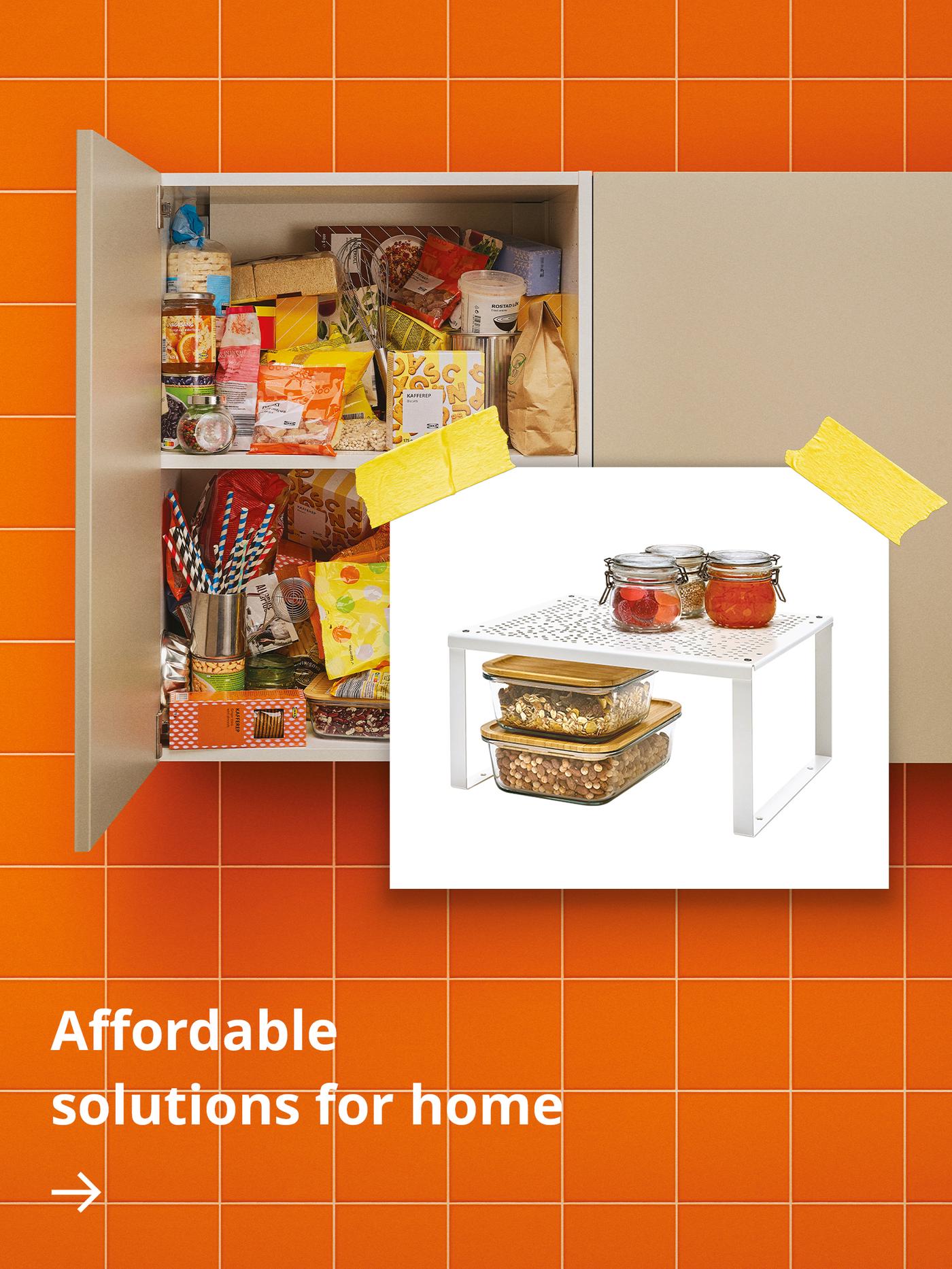 A wall-mounted kitchen cabinet set against orange tiles stands open, revealing packets, spices and other everyday items neatly organised on a VARIERA shelf insert.
