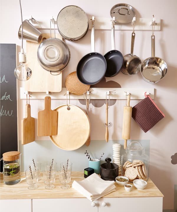 A wall of pots, pans and cooking utensils, hanging from hooks in a small white kitchen.