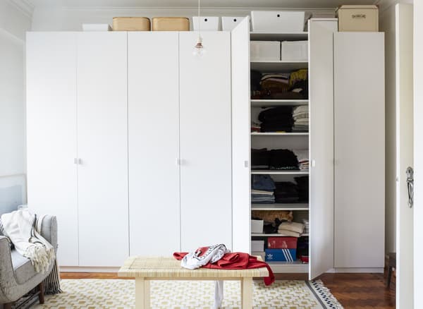 A wall of white wardrobes with storage boxes on top and a rattan coffee table in front.