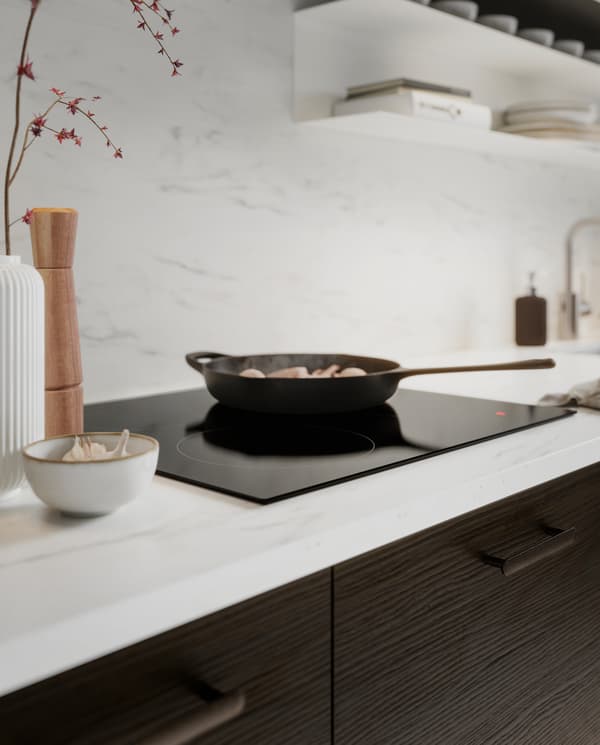 A wall panel/worktop in white marble effect, kitchen fronts in dark brown ash effect, an induction hob and a cast-iron pan.
