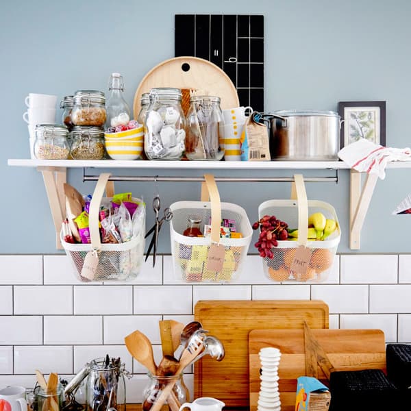 A wall shelf and three baskets filled with containers of dry food stuff and fruit. 