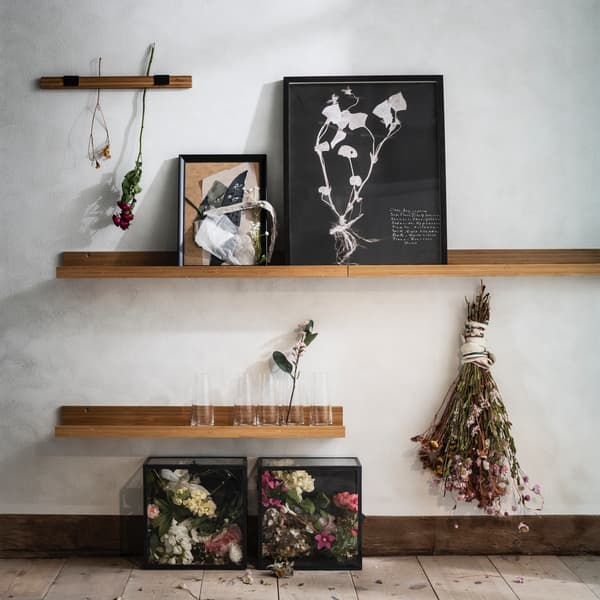 A wall with wall shelves displaying art and dried flowers.