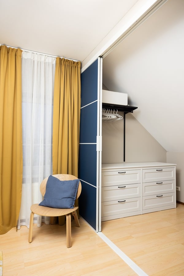 A wardrobe area partially open, showing drawers and hanging space behind sliding doors in a children’s attic room.