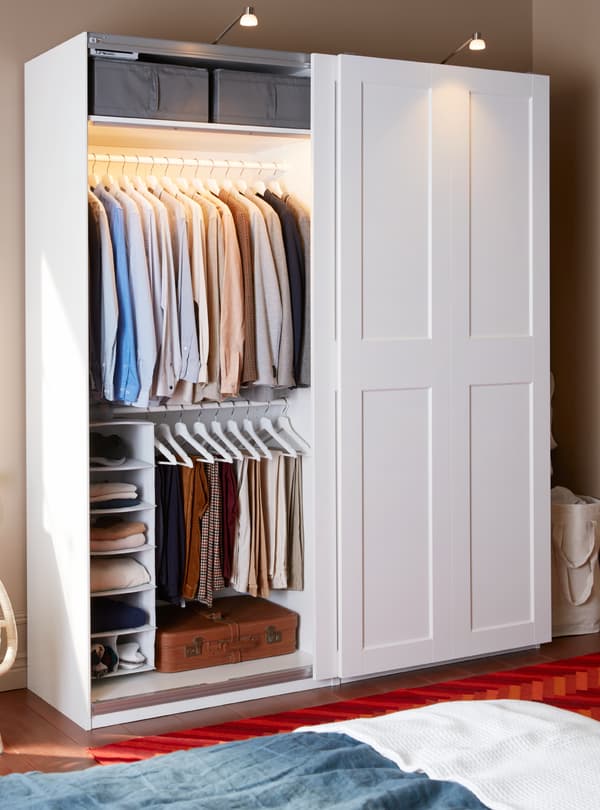 A wardrobe in light wood filled with clothes on shelves but also hanging on hangers.