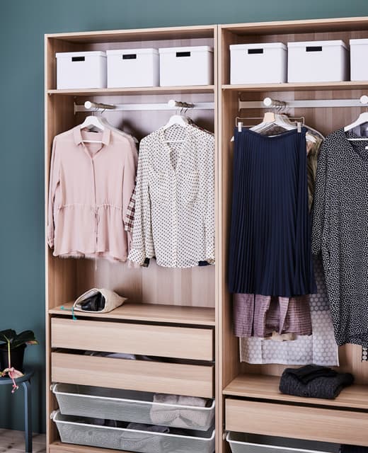 A wardrobe is organized with drawers, hangers and paper boxes on the top shelf.