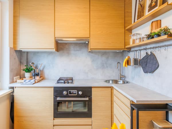 A warm and modern kitchen after the makeover, featuring cabinets with light wood fronts, a built-in oven, sleek worktops, open shelving and contemporary decor.