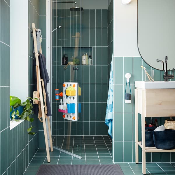 A wash-stand/wash-basin in birch/white, an oval mirror, a towel stand in birch, three blue baskets and a glass shower door.
