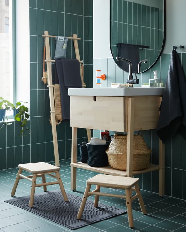 A wash-stand/wash-basin in birch/white, two step stools in birch, an oval mirror and a hand towel in dark grey.