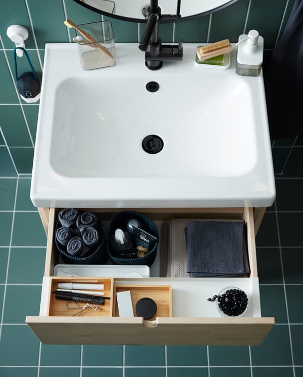 A wash-stand/wash-basin in birch/white with an open drawer. Towels and makeup are organised on trays and in baskets.