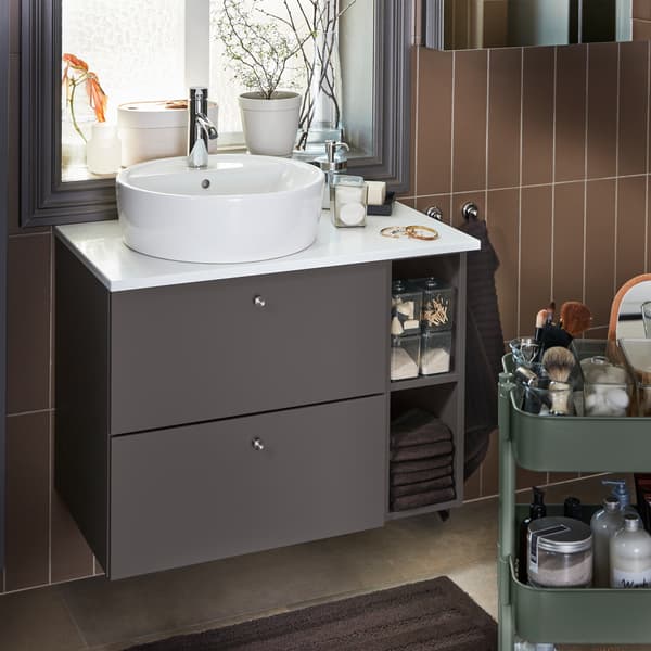A wash-stand/wash-basin in dark gray/white, towels and a bath mat in dark brown and a gray-green trolley.