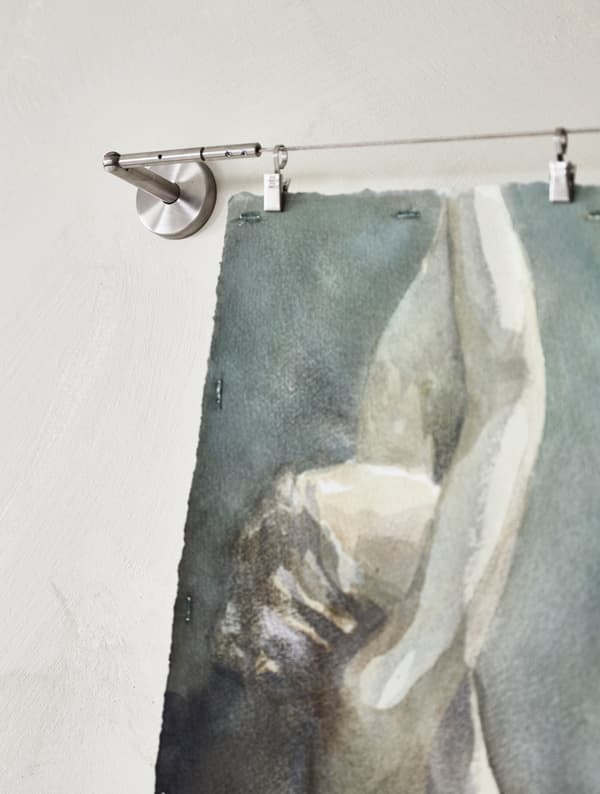 A water colour painting hung to dry from a wire curtain hanger.