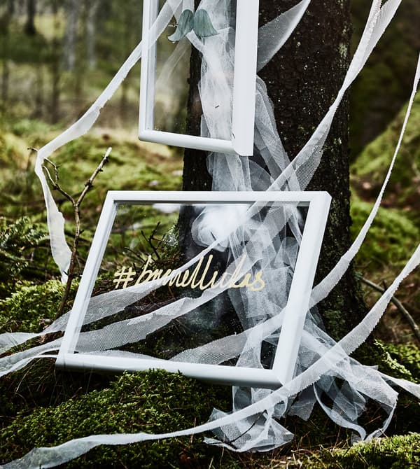 A wedding hashtag painted on the clear plastic glass of a  frame for a DIY wedding photobooth